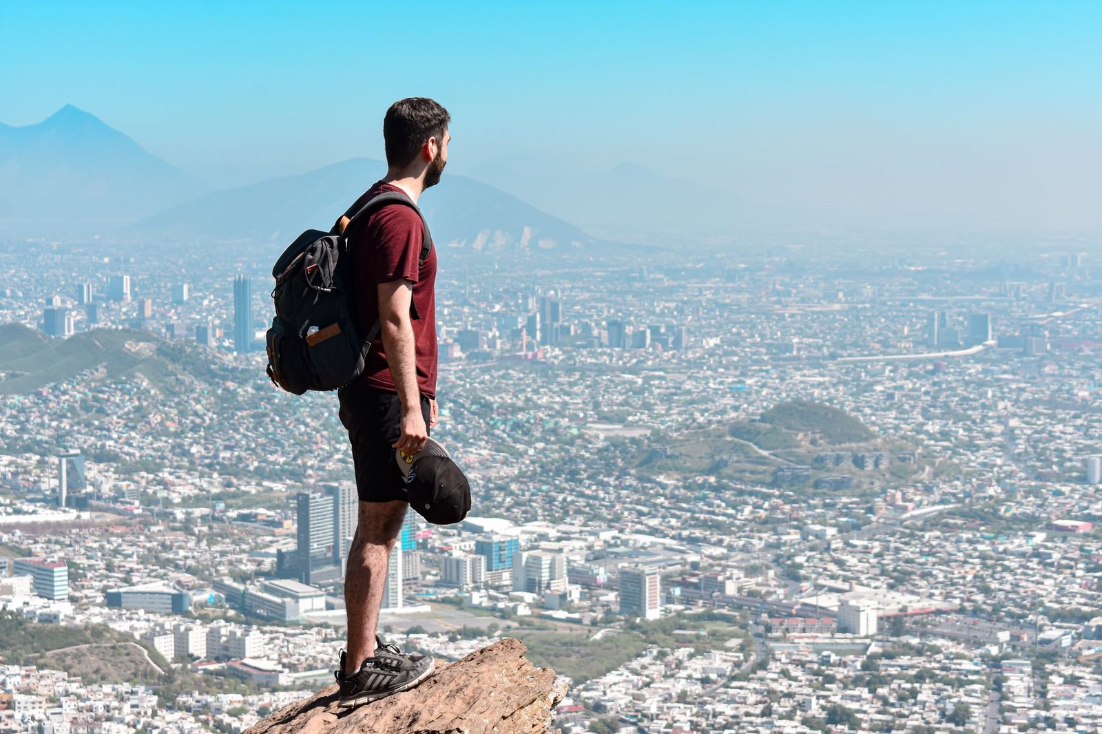 man with backpack standing on rock over city
