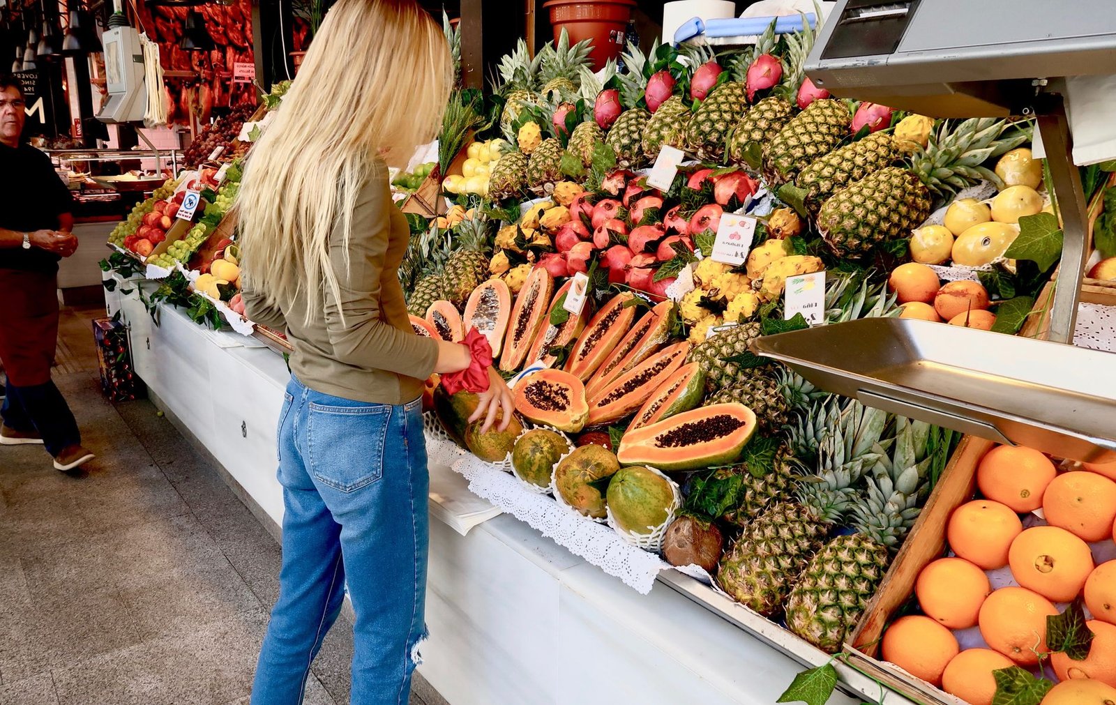 a woman in brown long sleeve shirt and blue denim jeans standing in front of fruit stand