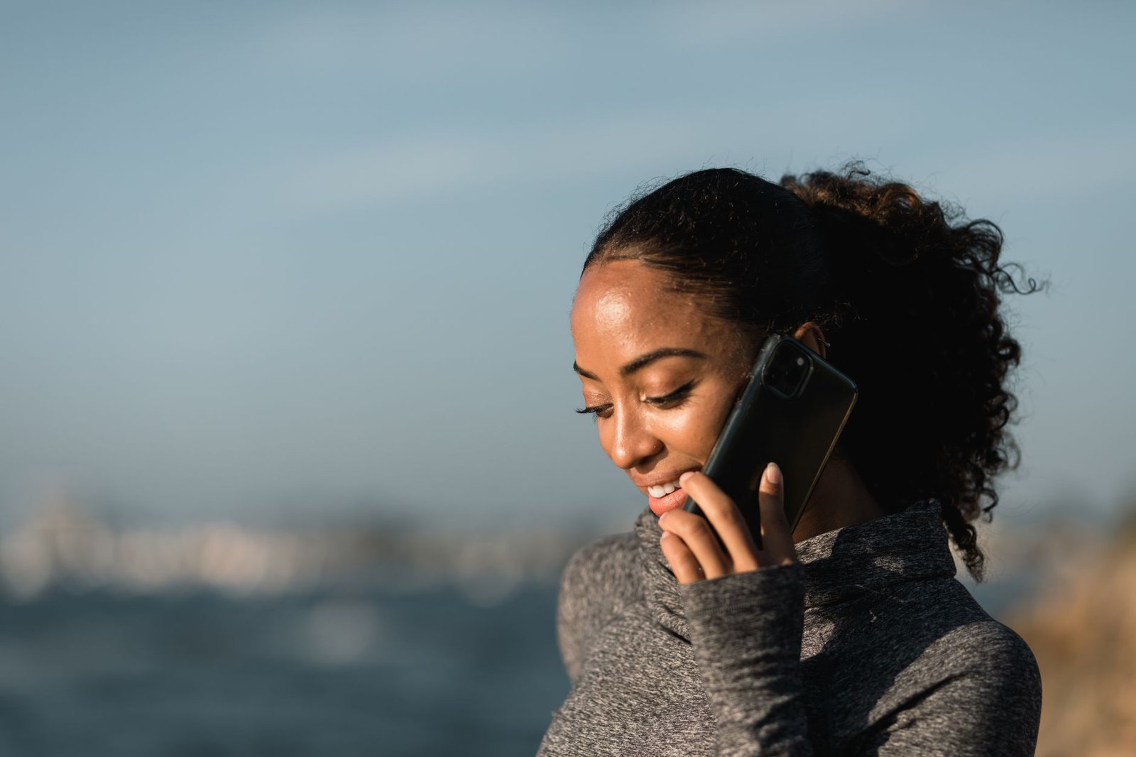 woman in gray sweater holding black smartphone