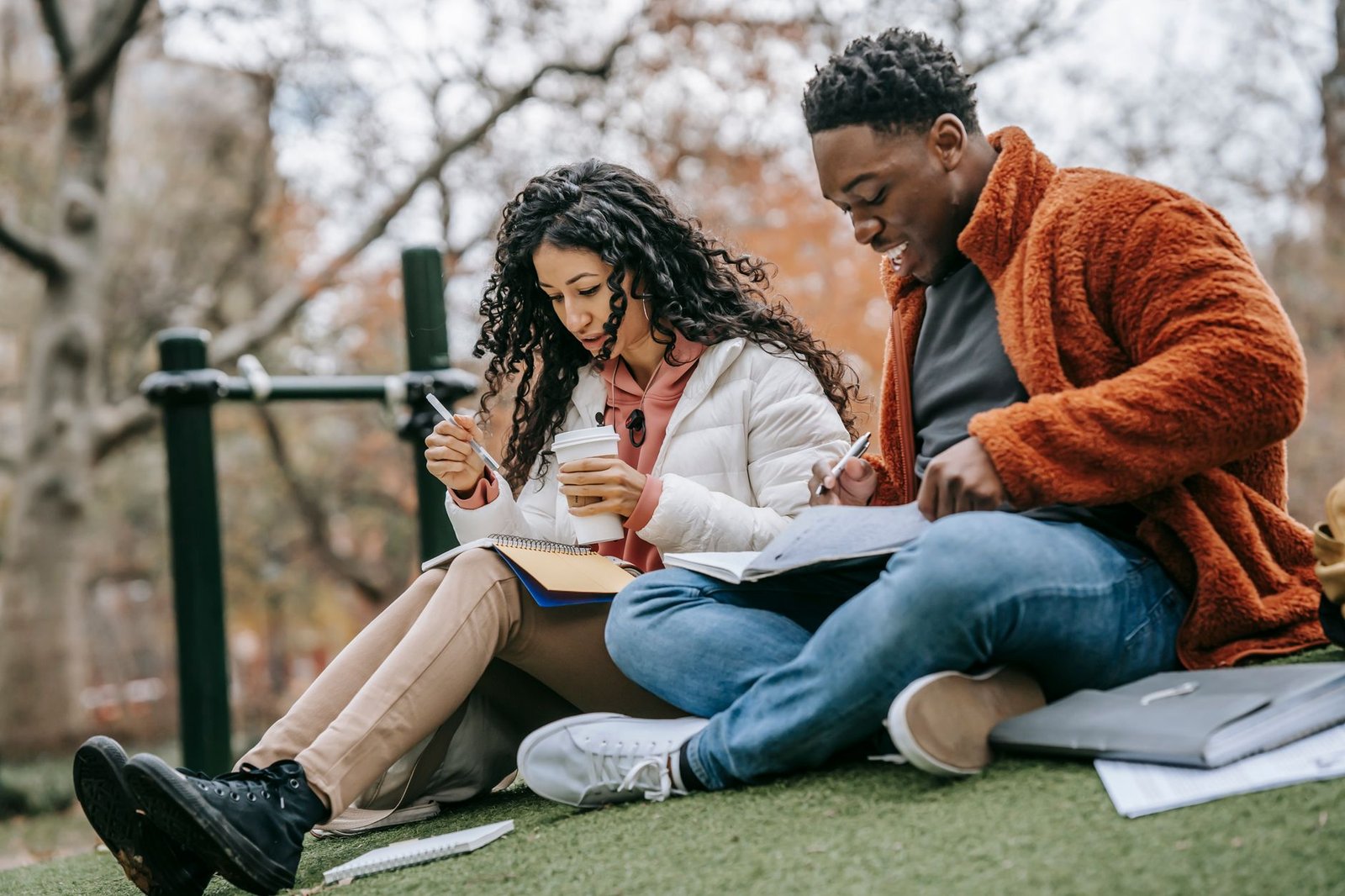multiethnic couple with copybooks studying on grassy lawn